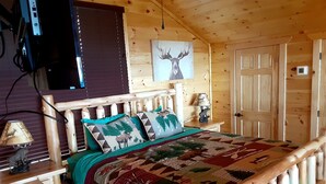 Et træhusværelse med seng, lampe, et billede af en elg og en dør.