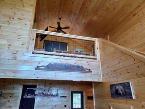 A wooden cabin interior with a balcony, a ceiling fan, and a mural of a bear.