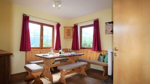 Une table à manger en bois, avec des bancs, des rideaux rouges et une vue par les fenêtres.