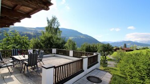 Une terrasse extérieure avec une table et des chaises, entourée d’une clôture en bois, offrant une vue sur un paysage montagneux.