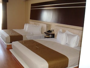 A hotel room with two beds, each with white linens and brown headboards. There is a bedside table with a phone and a lamp.
