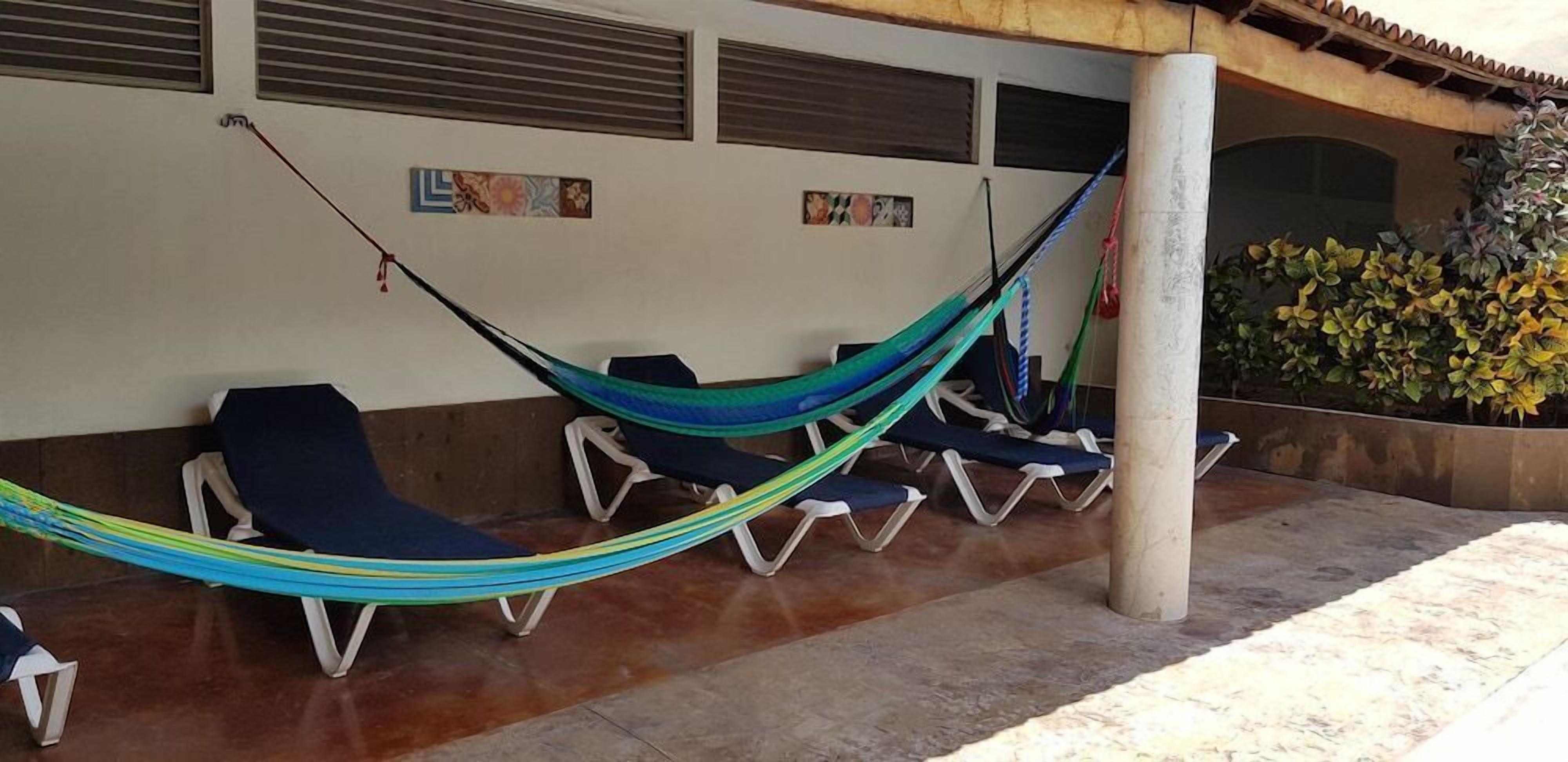 Un hamac tendu entre deux chaises longues, à l’extérieur d’un bâtiment dont le sol est recouvert de carreaux et qui possède une colonne.