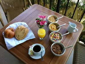 A breakfast table with croissants, juice, cereal, coffee, and flowers.