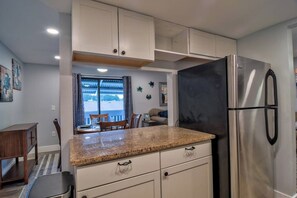A compact kitchen with white cabinets, a stainless steel refrigerator, and a granite countertop.