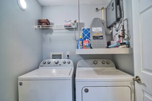 A laundry area with two white front-loading washers and dryers, a shelf with laundry supplies, and a wall-mounted ironing board. - *Coastal 2/2 Condo w/ Pool 6 Mins to IMG (Bradenton)