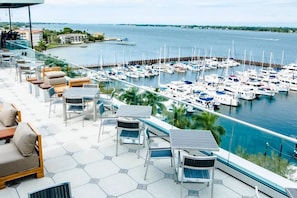 A marina with boats docked, a glass balustrade, and outdoor seating with chairs and tables. - *Coastal 2/2 Condo w/ Pool 6 Mins to IMG (Bradenton)
