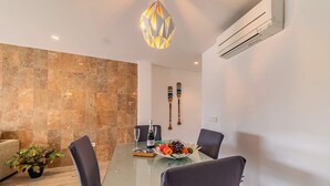 Un comedor moderno con una mesa de vidrio, sillas oscuras, un centro de mesa decorativo con frutas y una lámpara colgante geométrica original.