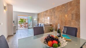 Una sala moderna con una mesa de vidrio, un sofá y un comedor con un frutero y un libro.