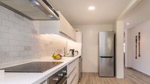 Una cocina moderna con armarios blancos, un refrigerador de acero inoxidable y una cocina de inducción negra.