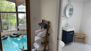 Une salle de bain avec vue sur une piscine extérieure, une étagère en bois avec des serviettes, un lavabo et un miroir.