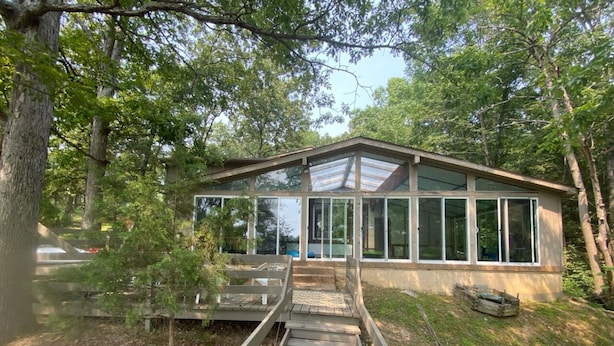Un bâtiment moderne doté de grandes fenêtres, d’une terrasse en bois et d’un chemin menant à l’entrée.