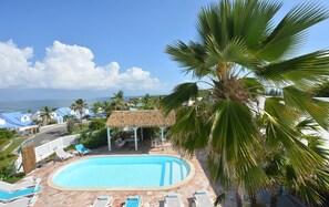 A pool area with lounge chairs and a thatched-roof structure, overlooking a beach and ocean. - SINGLE-FAMILY VILLA WITH OCEAN VIEW (OYSTER POND)
