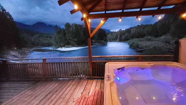 Ein Whirlpool auf einer Holzterrasse mit Blick auf einen Fluss und Berge.