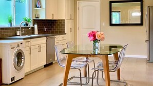 Une cuisine moderne équipée d’un lave-linge et d’un sèche-linge intégrés, une table à manger en verre avec des chaises, et un vase de fleurs posé sur la table.