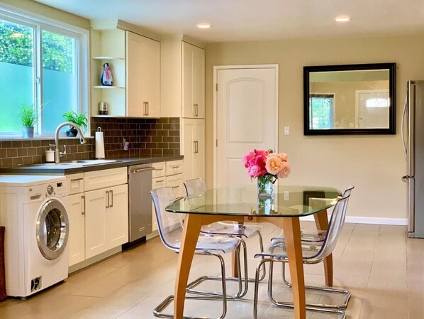 A modern kitchen with a built-in washer and dryer, a glass dining table with chairs, and a vase of flowers on the table.