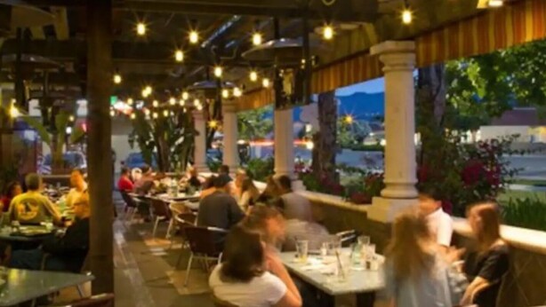 Un restaurant en plein air avec des tables et des chaises, des guirlandes lumineuses et une vue sur le paysage urbain.