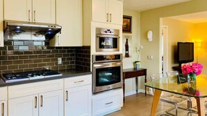 Une cuisine moderne avec des meubles blancs, une cuisinière à gaz, une hotte aspirante et deux fours.