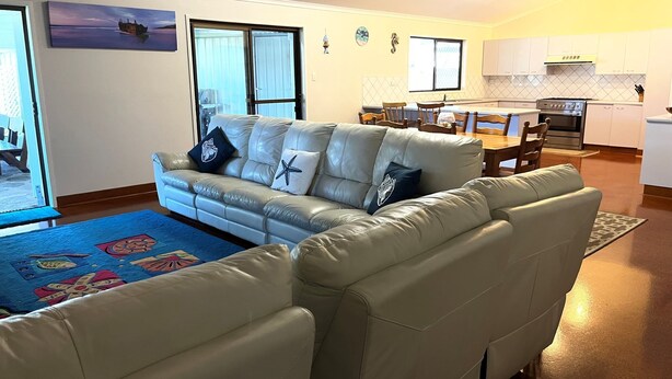 A living room with a sofa, a dining table with chairs, and a kitchen area with a stove and cabinets.