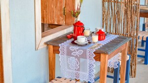 A wooden table with a lace tablecloth, red teapots, and a vase with flowers. - EcoCharme Pousada Netuno (Fernando de Noronha)