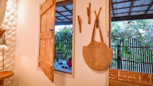 A room with a wooden door, a window with a view of greenery, and a woven bag hanging on the wall. - EcoCharme Pousada Netuno (Fernando de Noronha)