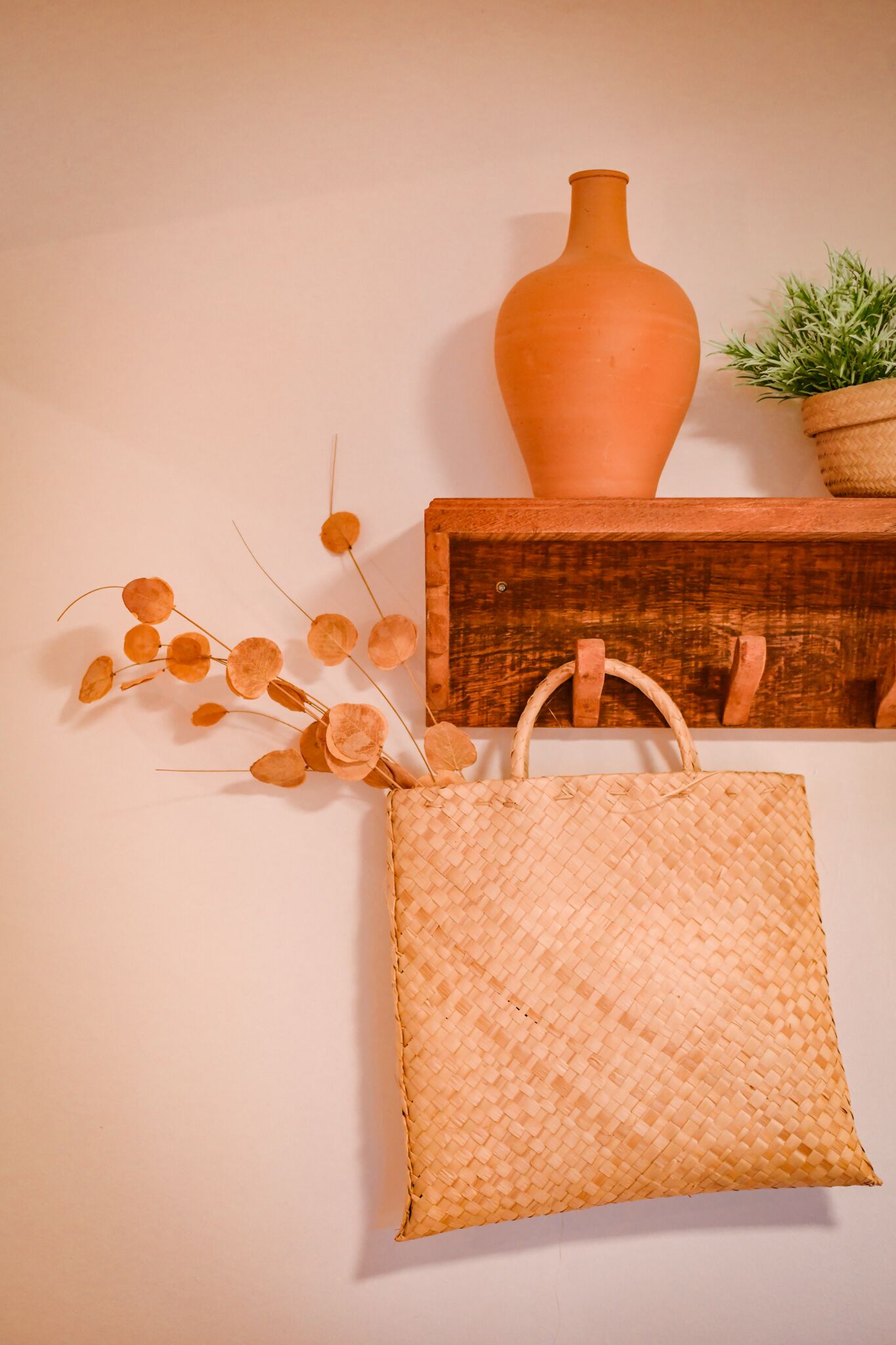 Un bolso tejido colgado en una pared, una maceta de terracota y una pequeña planta en maceta.