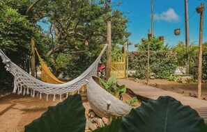 Un hamac tendu entre deux arbres, une terrasse en bois et un portail jaune.