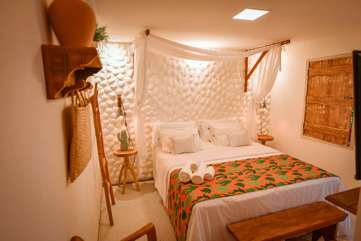 A cozy bedroom with a bed, a bench, a small table, and a wall-mounted shelf.