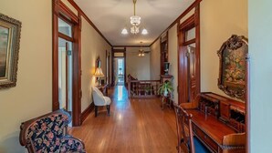 A spacious hallway with wooden flooring, a chandelier, and a piano.