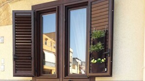 A wooden table with chairs, a basket of flowers, and a cactus plant outside a building with a brown door and window shutters. - Charming tourist apartment (Bagheria)