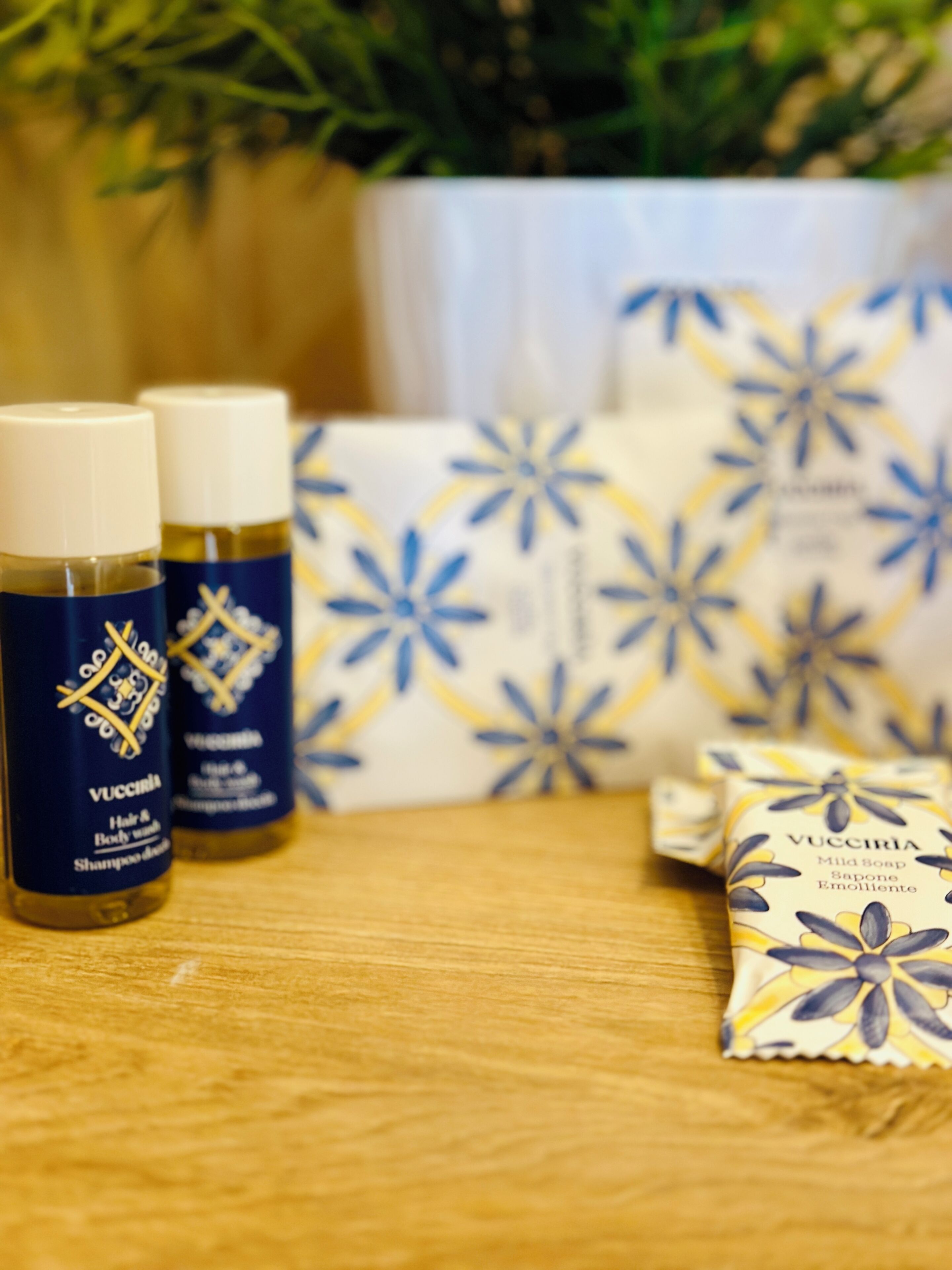 A wooden surface with two bottles of Vucciria hair and body wash, a bar of soap, and a patterned box.