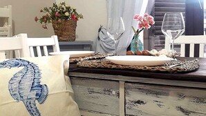 A dining area with a rustic wooden table, white chairs, and a decorative pillow with a seahorse design. - Charming tourist apartment (Bagheria)