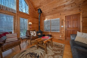 A cozy log cabin interior with a fireplace, leather furniture, and large windows.