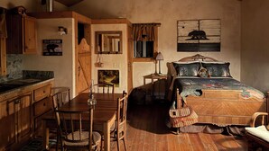 Interior rústico de una cabaña con una mesa de comedor de madera, una cama con un cabecero decorativo y una araña hecha de astas de ciervo.