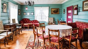 A room with a wooden floor, a red sofa, a round table with a lace tablecloth, and a chandelier.