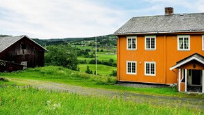 A rural landscape with a wooden barn and a bright orange house with a porch.