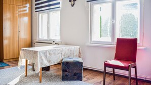 A room with a wooden wardrobe, a table with a floral tablecloth, a red chair, and a window with a view of trees. - 4 bedroom awesome home in Kobylnica (Kobylnica)