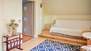 A room with a wooden door, a small table with a vase of flowers, a patterned rug, and a sofa with a blanket. - 4 bedroom awesome home in Kobylnica (Kobylnica)