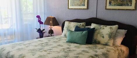 Un dormitorio con una cama, un ventilador de techo, una ventana con cortinas y dos cuadros en la pared.