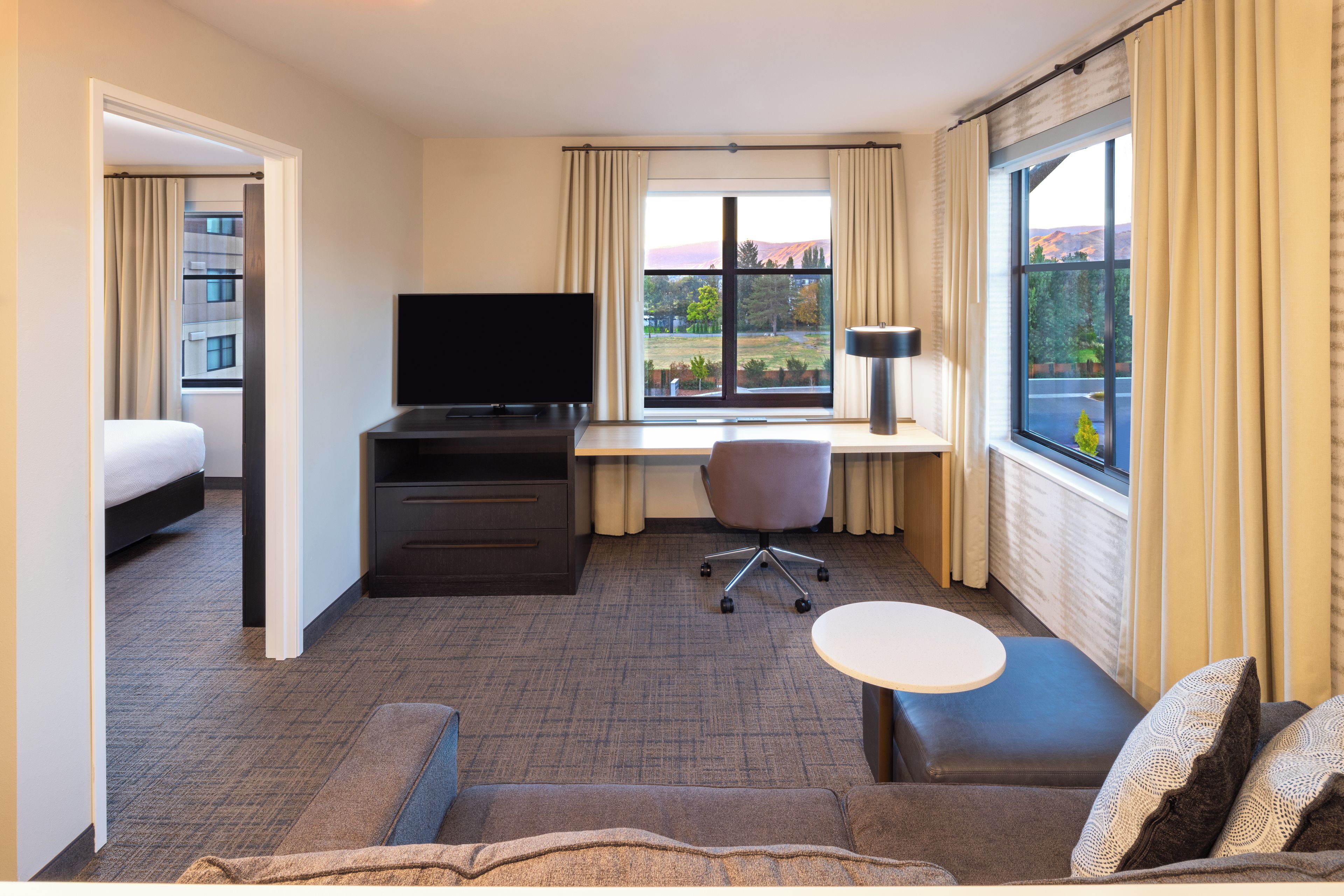 A hotel room with a bed, a desk with a computer, a television, a chair, and a small table.
