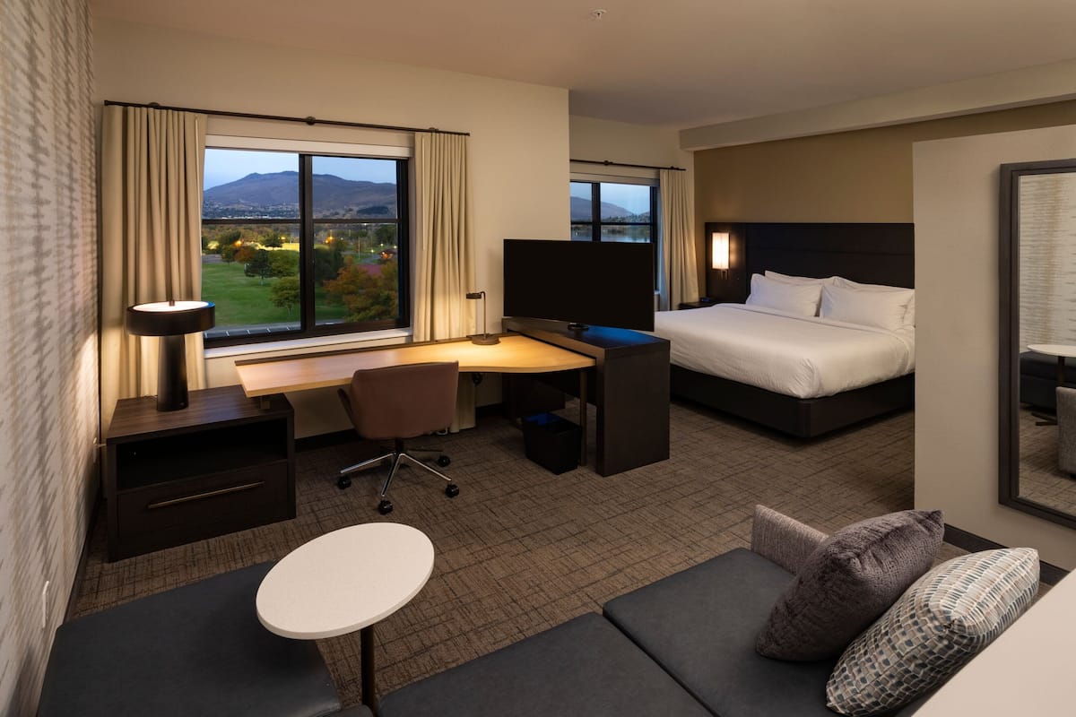 A hotel room with a bed, a desk with a computer, a TV, a sofa, and a view of the outdoors.