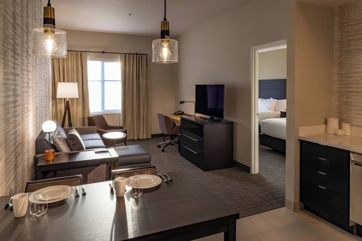 A hotel room with a dining area, a sofa, a TV, a bed, and a kitchenette.