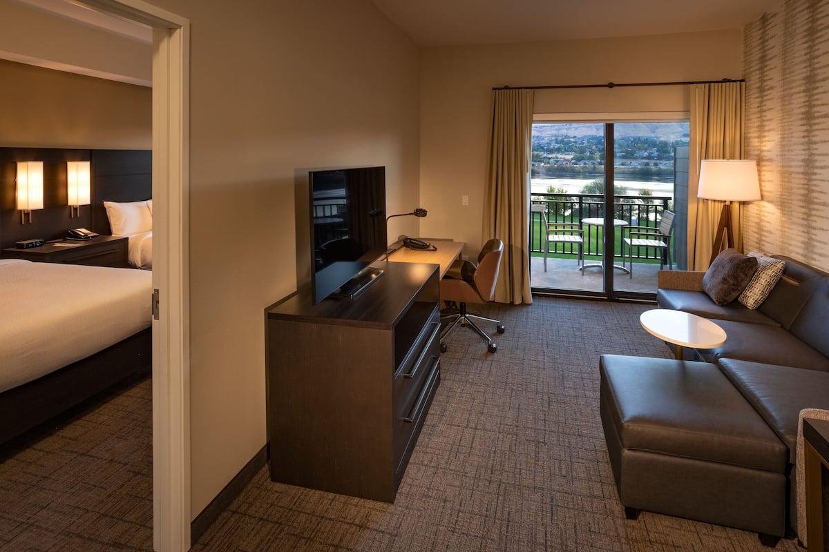 A hotel room with a bed, desk, chair, sofa, and a balcony with a view.