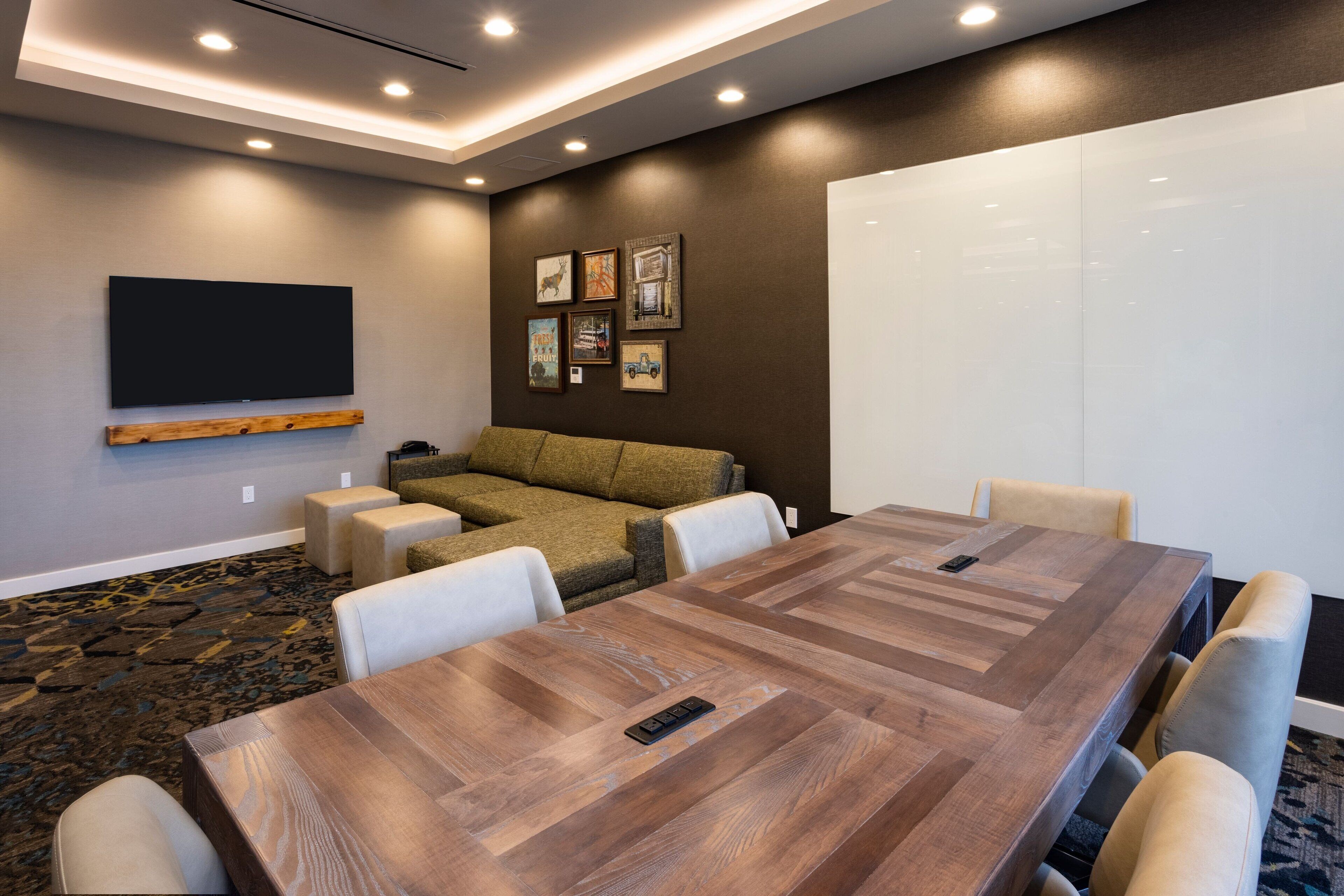 Ein Konferenzraum mit einem großen Holztisch, weißen Stühlen, einer Couch und einer Whiteboard-Tafel.