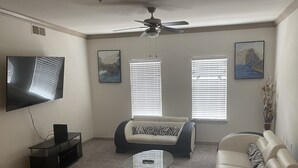 A living room with a ceiling fan, a flat-screen TV, two sofas, a glass coffee table, and two windows with blinds. - One Bedroom Peachtree Atlanta GA (Dunwoody)