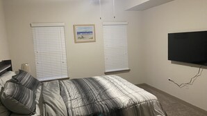 A bedroom with a bed, two windows with blinds, a ceiling fan, a wall-mounted TV, and a framed picture on the wall. - One Bedroom Peachtree Atlanta GA (Dunwoody)