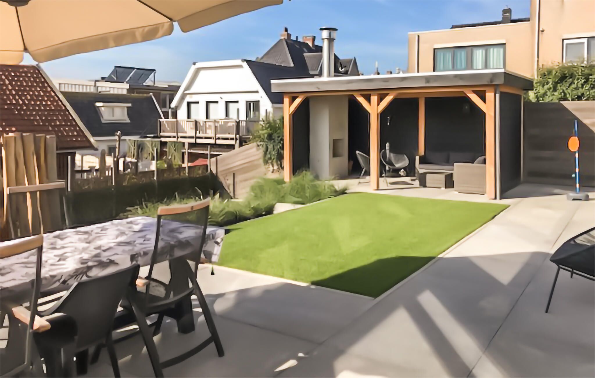 A patio area with a table and chairs, a green lawn, and a covered seating area with a view of neighboring houses.