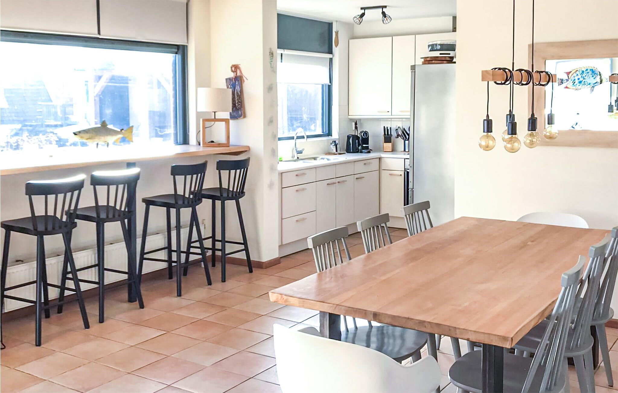 Een moderne keuken met witte kasten, een houten eettafel en barstoelen.