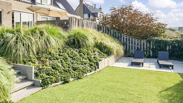 Een modern huis met een schuin dak, een verzorgd gazon en een houten omheining.