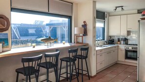 Een moderne keuken met witte kasten, een groot raam en een bar met zwarte barkrukken.