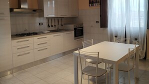 A modern kitchen with white cabinets, a gas stove, an oven, and a dining table with chairs. - Spacious apartment near the beaches and at the foot of Mount Etna (Mascali)